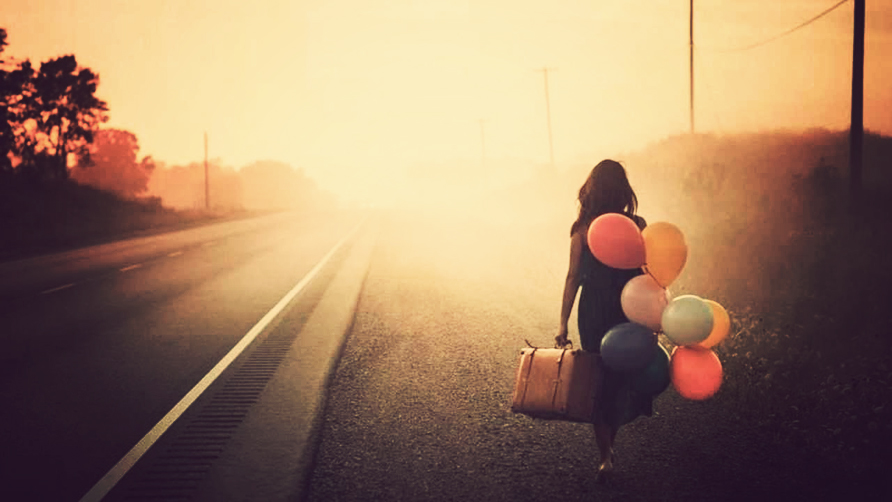 woman-walking-along-the-road-with-suitcase-and-balloons